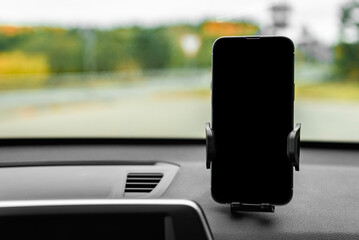 Car holder with mobile phone with black screen on windshield of car.
