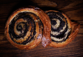Two delicious buns with poppy seeds lie on a wooden background.