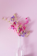 Empty wine bottle with colorful party streamers on a pink pastel background. Minimal New Year party...