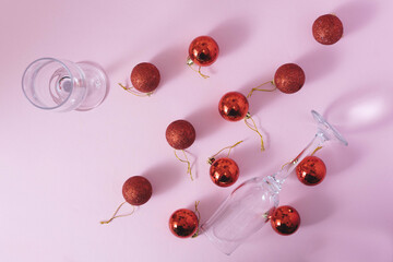 New Year party background with glasses and red Christmas baubles on a pink pastel background. Christmas celebration and New Year idea. Flat lay.