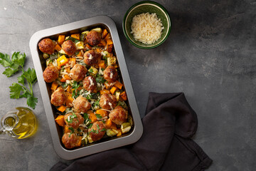 Meatballs on a vegetable bed of pumpkin and zucchini on a baking sheet and gray background, copy space for text - obrazy, fototapety, plakaty