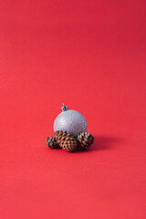 Christmas decorations a silver bauble and brown cone against a red background. New year minimal concept.
