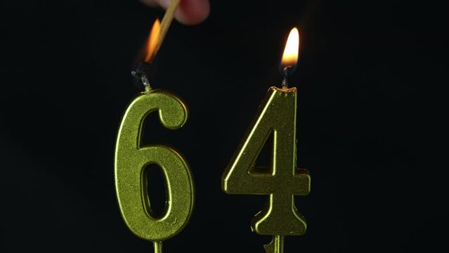 close up on the gold number sixty-fourth candle on a dark background.

