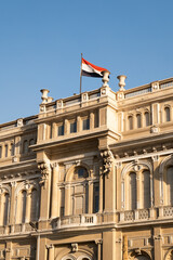 Fototapeta na wymiar Egyptian flag waving on top of a government building with the blue sky behind