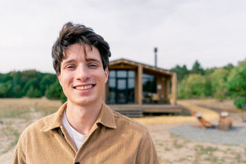 Portrait of a young smiling lad against the background of large wooden cottage in the forest steppe 