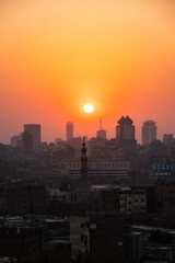 Fototapeta premium Orange and yellow open skies. Sunset over the city of Cairo in Egypt. Silhouette of the buildings in the metropolis. Neighborhood view of the cityscape.