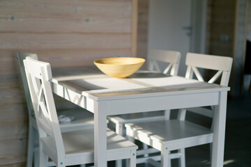 The rays of the sun illuminate a light table and several chairs that stand in spacious kitchen in...