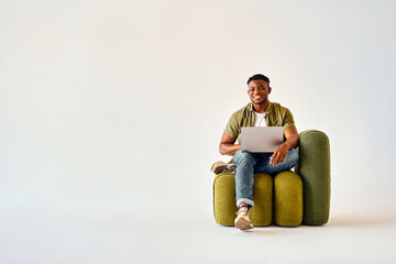 Positive african american man in casual wear sitting on design green chair and working on portable...