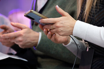 Woman using smartphone sitting indoors, mobile phones in people hands close up. Concept of briefing, business meeting or conference