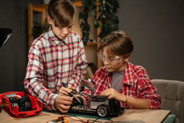 Teenage brothers studying electronics making a car on the remote control in their room, working on a science project