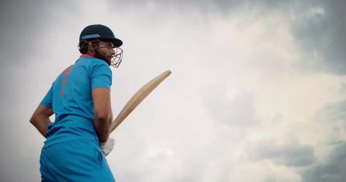 Professional Indian Cricket Player Striking the Ball with a Bat. Batter From a Blue Team Successfully Hits the Ball to the Outfield. Low Angle Action Footage on a Cloudy Day