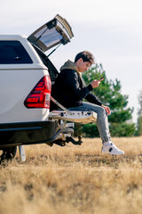 A guy sits in the trunk of a car while traveling through beautiful places in forest and steppe © Guys Who Shoot