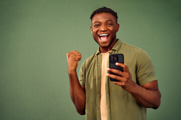 Big luck. Portrait of happy afro young man using modern smartphone and making winner gesture over...