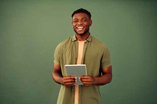 Online Education. Positive african american guy in casual khaki shirt standing over green studio background with digital tablet in hands. Happy male student using modern gadget for distance learning.