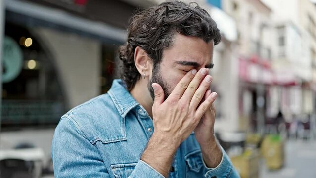 Young hispanic man rubbing the eyes at street