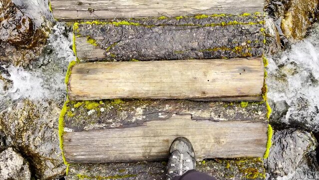 Slow motion 4K video POV view of Man's legs in trekking boots crossing mountain creek by wooden bridge during Makalu Barun National Park trek in Nepal. Mountain hiking and active people concept image.