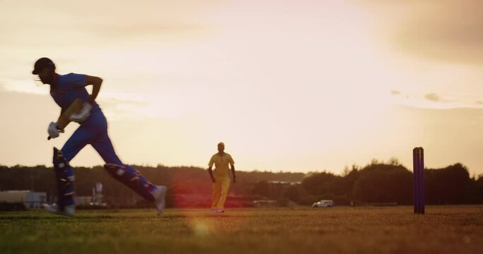 Professional Indian Cricket Player in Blue Uniform and Protective Gear Hitting the Ball and Defending the Wicket. Athletes Practicing on a Green Field on a Sunny Afternoon. Cinematic Slow Motion