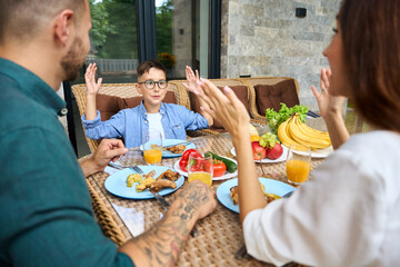 Mother and father communicate with their son over lunch on terrace