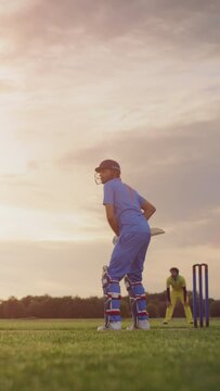 Vertical Screen: Professional Cricket Player in Blue Uniform and Protective Helmet and Pads Preparing to Hit the Ball and Win the Match. Two Young College Teams Practicing on a Warm Sunny Evening