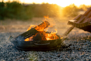 Close-up shot of a fire with wood burning at sunset near a cosy wooden house in countryside