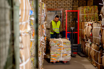 A worker using a stacker lifts and transports a cargo cardboard box with things for recycling at...