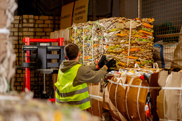 A male employee using stacker takes out a paper box with used items to be transported and sent for...