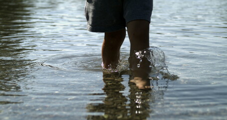 Child feet walking in lake shore water