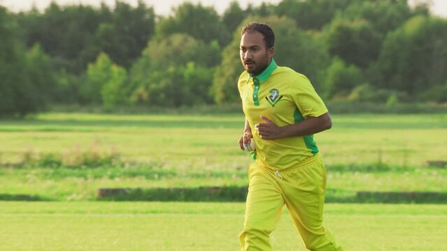 Slow Motion Portrait of a South Asian Cricket Player in Yellow and Green Uniform Throwing the Ball on a Pitch. Professional Indian Bowler is Focused, Aiming to Hit the Wicket With His Shot
