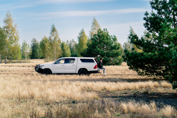 The car is standing on the road in the forest-steppe A young guy sits in the open trunk with phone...