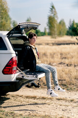 Naklejka premium A guy sits in the trunk of car while traveling through beautiful places in forest and steppe