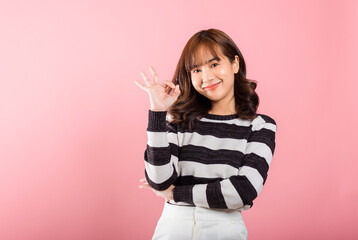 A smiling woman displays the OK sign to agree in a studio shot on a white background. Happy Asian portrait of a young female with a positive hand sign and copy space.