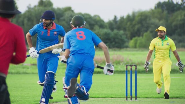 Professional Indian Cricket Player in Blue Uniform and Protective Gear Hitting the Ball and Defending the Wicket. Athletes Practicing on a Green Pitch on a Warm Afternoon