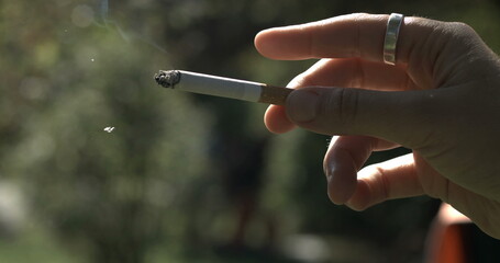 Finger tapping into cigarette ash falling off captured in. Close-up hand holding addictive substance