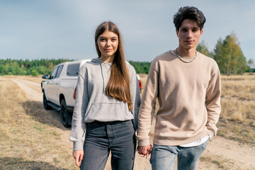 Obraz premium A young couple a girl and a guy walk together in the forest steppe holding hands and talking against backdrop of their car