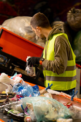 Side view of a sorter in gloves and a protective vest who sorts garbage on a special sorting line while working at waste disposal station