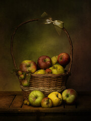 Dark still life image of windfall apples from local orchard in a basket. Assorted varieties, imperfect specimens.