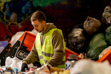 Side view of a sorter in gloves and a protective vest who sorts garbage on a special sorting line...