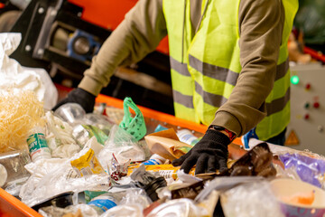 Hands in gloves of a uniformed employee sort garbage into categories on a special line at waste...