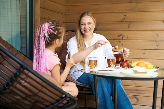 Beautiful mother sincerely laughing pouring fresh warm tea into daughter cup - Powered by Adobe