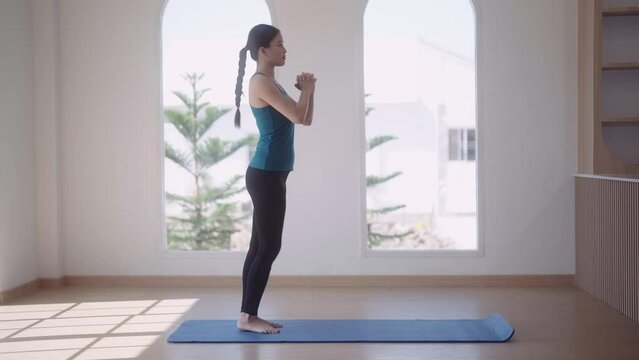 An Asian young woman in workout attire is exercising by stretching her legs forward on a mat for a healthy workout routine at her home, strengthening her overall health