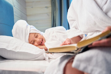 Obraz premium Caring mother reading book with funny stories to her little daughter