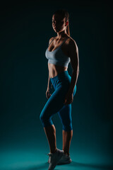Fit woman demonstrating her muscular physique in a studio. Silhouette showing strength and motivation. She serves as an inspiration for body transformation and fitness goals.
