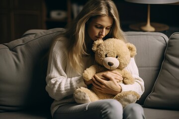 Nostalgic girl sitting on a sofa hugging a teddy bear