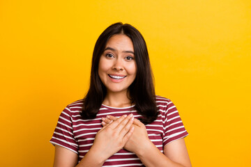 Portrait of thankful appreciative woman with straight hairdo dressed stylish t-shirt hold arms on chest isolated on yellow background