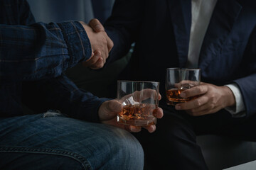 Close-up view of two men in formal attire clinking whiskey glasses, stylish businessman friends in suits toasting with whiskey glasses in home, closeup