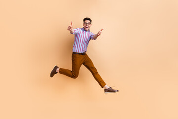 Fototapeta na wymiar Full length photo of cheerful satisfied man wear stylish clothes walking showing thumbs up cool job isolated on beige color background