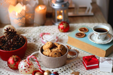 Various colorful Christmas decorations, soft blanket, cup of tea, sweet snacks and lit candles on the table. Cozy Christmas atmosphere at home. Selective focus.