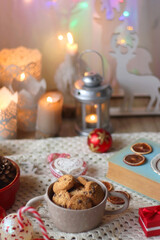 Various colorful Christmas decorations, soft blanket, cup of tea, sweet snacks and lit candles on the table. Cozy Christmas atmosphere at home. Selective focus.
