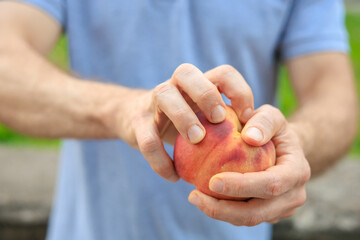 A man's hand holds a peach, snack and fast food concept. Selective focus on hands with blurred...