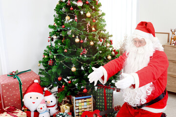 Santa Claus surrounded by gift boxes under Christmas tree, raising hands to give a hug to good children. Happy grandpa white beard Santa in red costume celebrating winter holiday. Merry Christmas